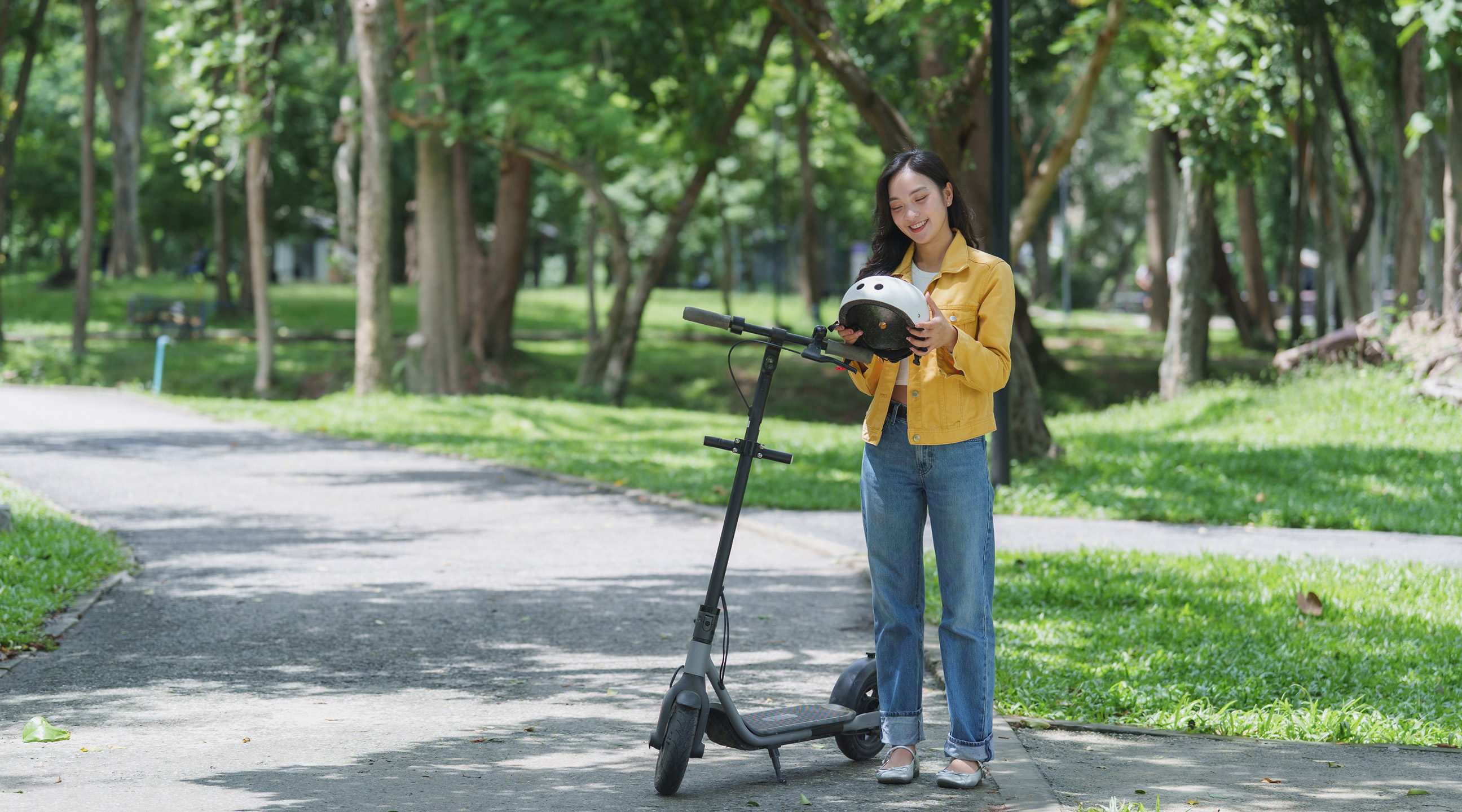Ragazza con il casco in mano accanto a un monopattino elettrico in un parco